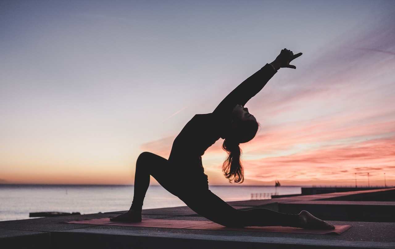 Silhouette of a person in a deep lunge yoga pose at sunset by the ocean