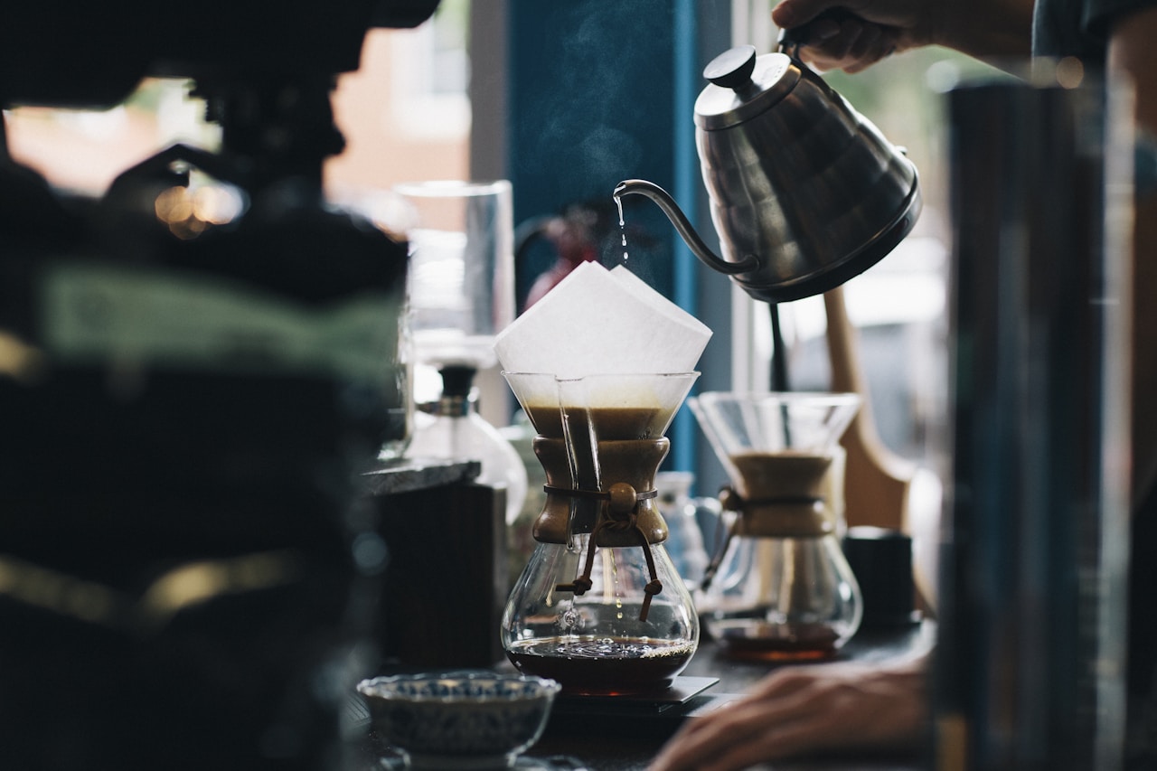 Pouring dark coffee from a pot into a cup on a wooden surface