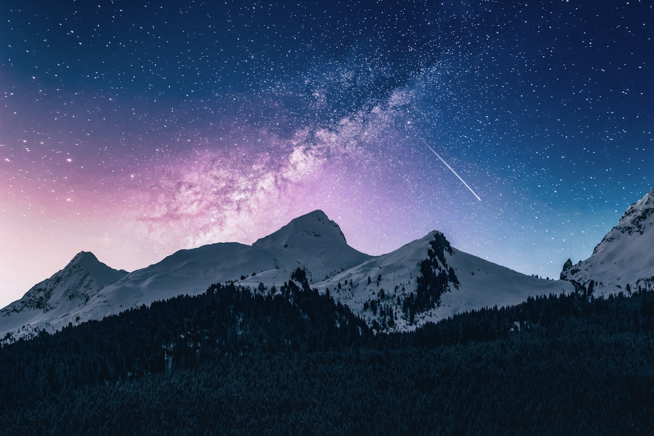 Milky way and starry sky above snow-covered mountains and dark forest