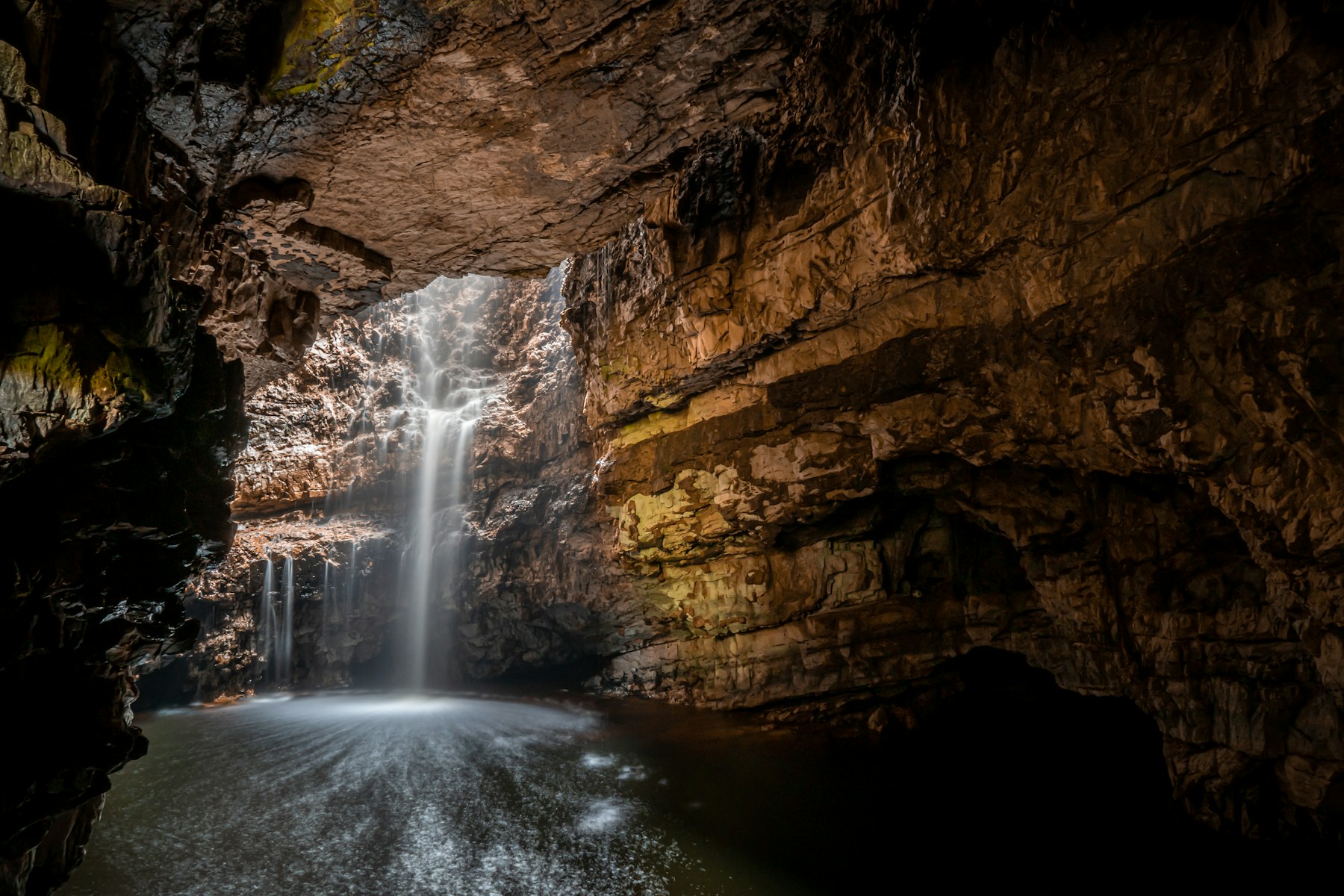 Underground waterfall plunging into a dark pool inside a limestone cave