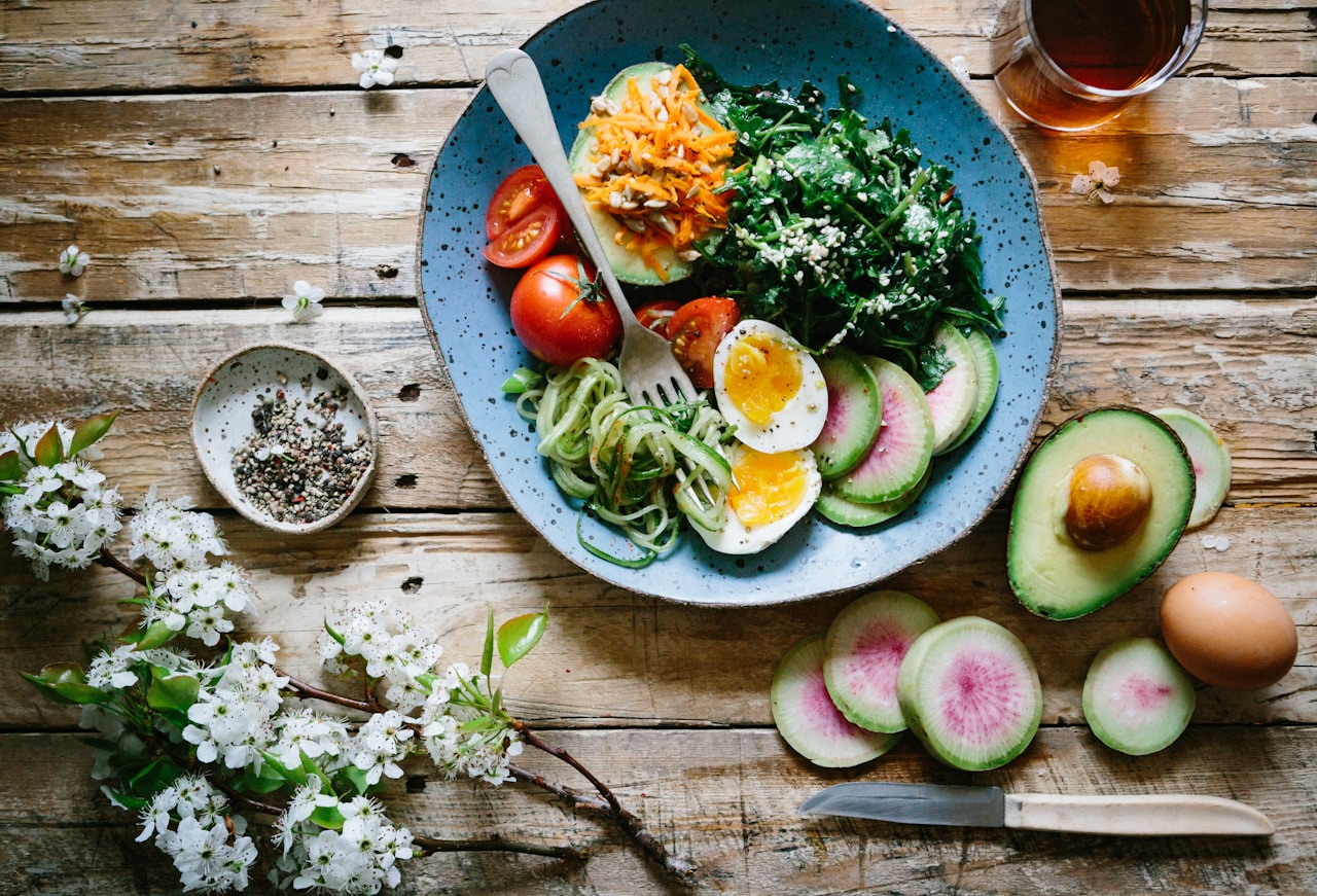 Colorful grain bowl with egg, avocado, greens, and vegetables on a wooden table