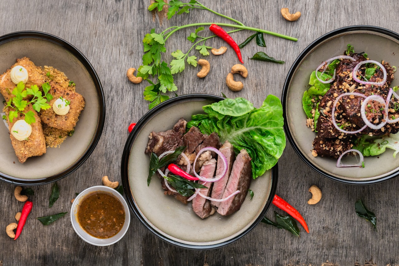 Three plated high-protein dishes with steak, breaded cutlets, and glazed meat on a wooden table