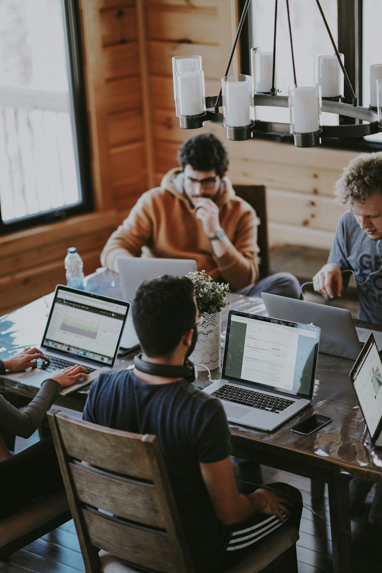 Four people working on laptops together at a wooden table in a cabin-style room